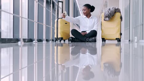 Woman-with-suitcases-is-sitting-in-the-airport-hall-and-taking-selfies