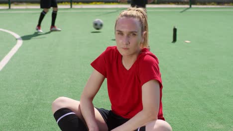 Female-Soccer-Player-Sitting-on-Playing-Field-and-Posing-for-Camera