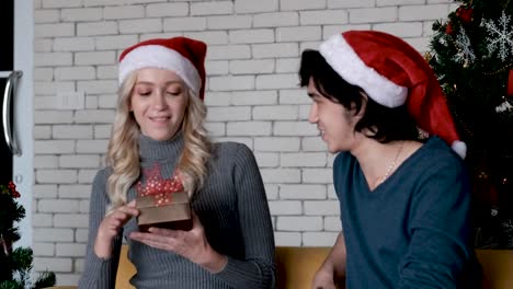 Young-man-give-the-Christmas-gift-to-his-young-girlfriend-in-the-room-with-Christmas-tree-as-background-in-concept-of-new-year-celebration