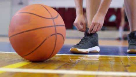 Low-Section-of-Female-Basketball-Player-Tying-Shoelace-and-Taking-Ball