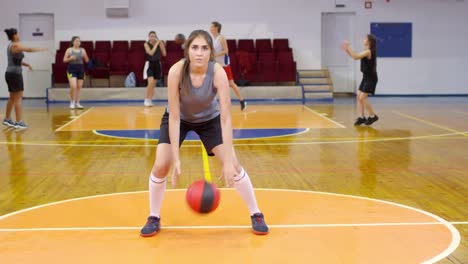 Junge-Sportlerin,-die-in-die-Kamera-schaut-und-einen-Basketball-dribbelt