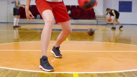 Atleta-femenina-mirando-la-cámara-y-regateando-un-baloncesto-entre-las-piernas