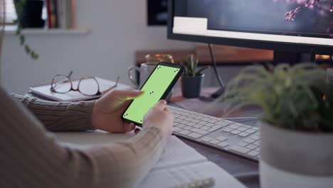 Mujer-anónima-usando-un-teléfono-inteligente-con-una-pantalla-verde-en-un-escritorio