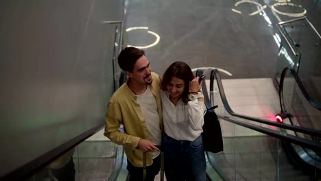 Loving-couple-on-the-escalator-at-the-airport.-A-guy-and-his-girlfriend-are-traveling-together.-Going-up-with-passports-and-suitcase-in-their-hands.-Happy-vacation-together