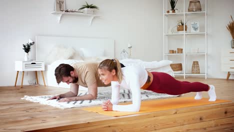 Young-couple-is-doing-plank-plank-exercise-at-home-in-cozy-bright-bedroom.-Stay-at-home-concept