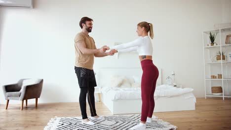 La-pareja-joven-está-haciendo-sentadillas-excercises-en-casa-en-acogedor-dormitorio-luminoso.-Concepto-de-estancia-en-casa