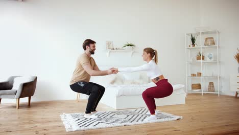 Young-couple-is-doing-squats-excercises-at-home-in-cozy-bright-bedroom,-slow-motion.-Stay-at-home-concept