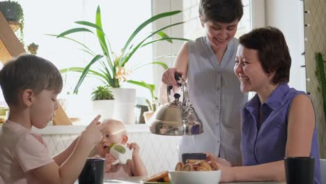 Eine-homosexuelle-lesbische-Familie-mit-zwei-Kindern-und-Müttern-sitzt-in-der-Küche-an-einem-Tisch-und-frühstückt.-Lebensstil.