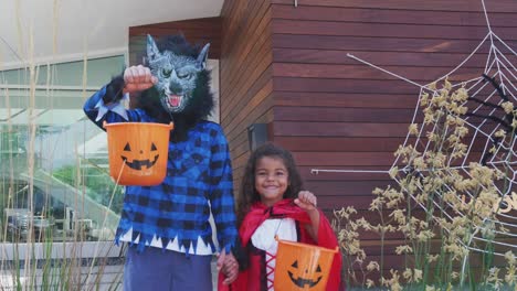 Portrait-Of-Two-Children-Wearing-Fancy-Dress-Outside-House-Collecting-Candy-For-Trick-Or-Treat