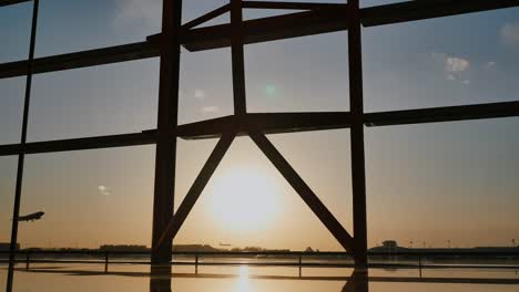 Silhouette-eines-Flugzeugs,-das-bei-Sonnenuntergang-am-Flughafen-Peking-im-Hintergrund-eines-Fensters-abstartet