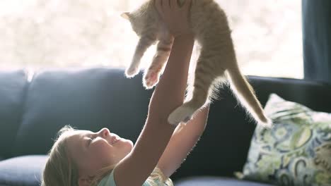 A-little-girl-holding-a-cat-up-above-her-head-and-then-giving-it-a-hug