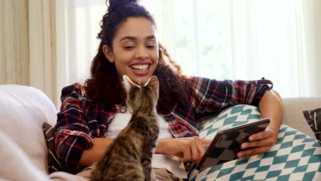 Feliz-mujer-sentada-en-el-sofá-con-su-tablet-al-gato-sentado-en-su-regazo-4K-4k