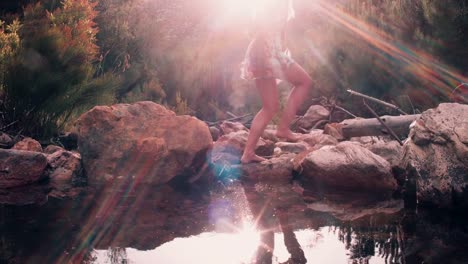 Girl-in-boho-floral-dress-stepping-over-stones-at-a-lake