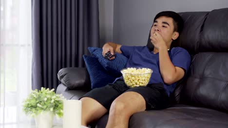 junger-Mann-Essen-Popcorn-auf-der-Couch-zu-Hause-sitzen-und-Fernsehen