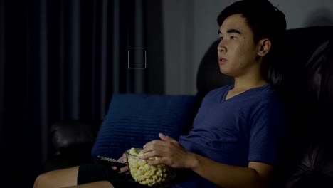 young-man-eating-popcorn-while-sitting-on-a-couch-and-watching-TV-at-night