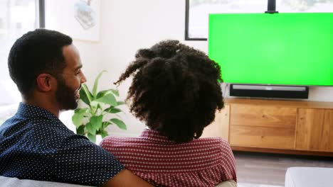 Vista-posterior-de-la-pareja-de-jóvenes-sentados-en-el-sofá-en-casa-y-viendo-la-televisión