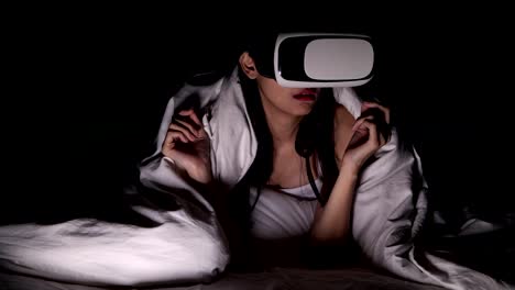 Woman-watching-VR-horror-movie-alone-in-bed.-Asian-woman-lying-in-bed-alone-wearing-VR-head-set,-very-surprise-and-shock-from-scary-movie.-High-tech-Halloween-home-alone-concept.