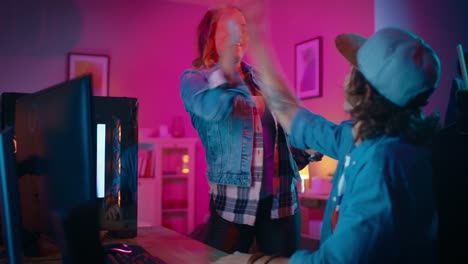 Two-Friends-or-a-Couple-Actively-Discuss-Something-on-a-Computer-Screen.-Pretty-Black-Girl-Points-to-the-Screen-and-Young-Man-Agrees.-They-High-Five.-Cozy-Room-is-Lit-with-Warm-and-Neon-Light.