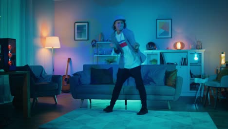 Handsome-Excited-Hip-Young-Man-is-Dancing-in-the-Living-Room-while-TV-Plays-in-the-Background.-He-is-Energetically-Moving-while-Screen-Adds-Reflections-on-Him.-Cozy-Room-is-Lit-with-Warm-Neon-Light.