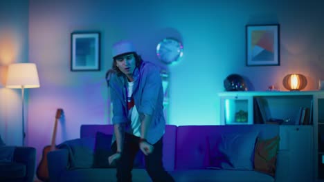 Handsome-Excited-Hip-Young-Man-is-Dancing-in-the-Living-Room-while-TV-Plays-in-the-Background.-He-is-Energetically-Moving-while-Screen-Adds-Reflections-on-Him.-Cozy-Room-is-Lit-with-Warm-Neon-Light.