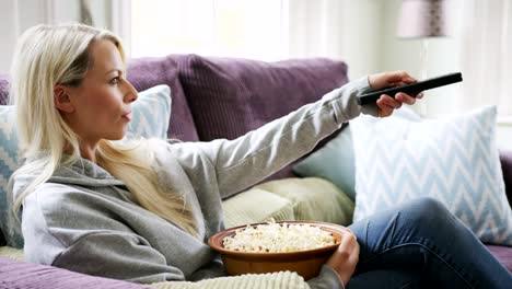 Schöne-blonde-Frau-mit-TV-Fernbedienung-auf-Sofa