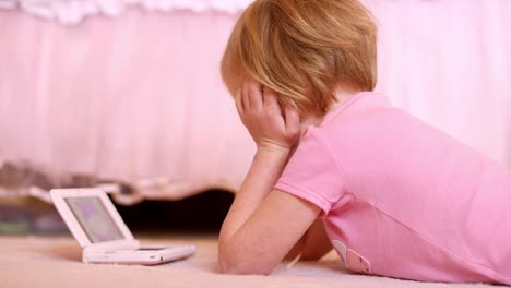 A-little-girl-laying-on-her-bedroom-floor-watching-a-show-on-her-handheld-gaming-system