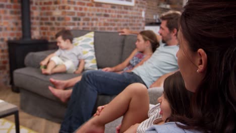 Family-Sit-On-Sofa-In-Open-Plan-Lounge-Watching-Television