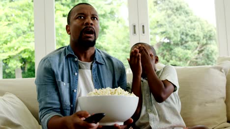 Son-covering-his-eyes-while-watching-television-with-father