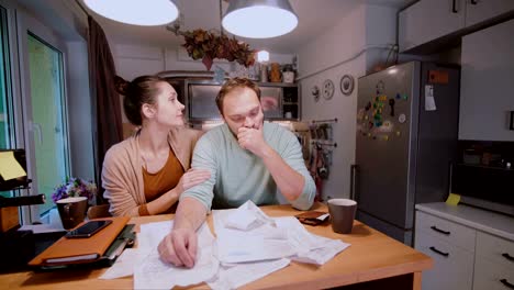 Worried-couple-looking-at-their-bills-in-the-kitchen-at-home.-Man-and-woman-calculating-domestic-accounts