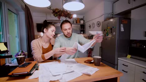 Young-couple-calculating-bills-in-the-kitchen-at-home.-Woman-try-to-calm-sad-and-angry-husband