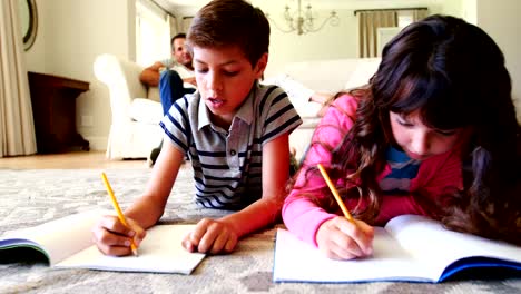 Siblings-doing-homework-while-lying-on-rug-in-living-room