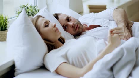 Closeup-of-couple-with-relationship-problems-having-emotional-conversation-while-lying-in-bed-at-home.-Young-woman-turn-away-her-boyfriend