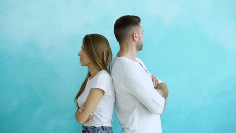 Young-couple-upset-and-angry-each-other-standing-rear-on-blue-background