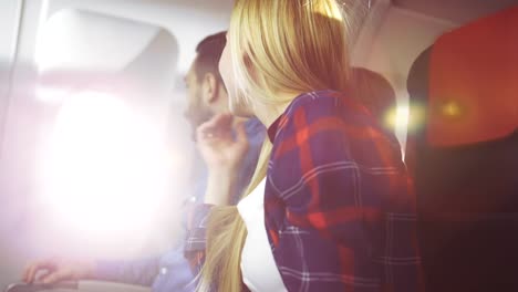 On-a-Commercial-Plane-Handsome-Young-Hispanic-Male-Opens-Window's-Shade-and-Hugs-His-Beautiful-Blonde-Girlfriend-and-they-Romantically-Look-Through-the-Window.-Sun-Shines-through-the-Porthole.