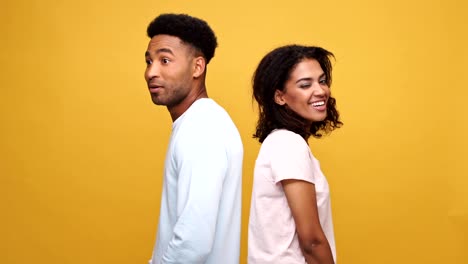 Young-african-couple-standing-back-to-back,-man-showing-disagreement-and-woman-showing-approval-gesture-isolated-over-yellow-background