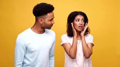 Young-african-couple-having-a-conflict,-woman-is-closing-her-ears-with-hands-isolated-over-yellow-background