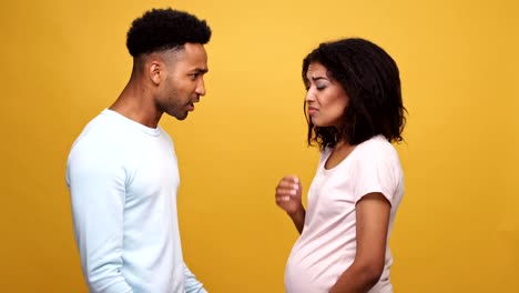 Angry-african-man-having-an-argument-with-his-pregnant-wife-and-she-begins-to-cry-isolated-over-yellow-background