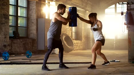Sportliche-Frau-Hits-Boxsack,-ihrem-Lebensgefährten-/-Trainer-hält.-Sie-ist-professionelle-Kämpfer-und-Training-in-einem-Fitnessstudio.