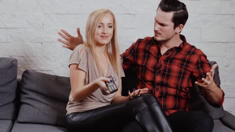 young-man-and-woman-are-sitting-on-the-couch,-watching-TV-and-holding-a-remote