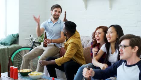 Multi-ethnische-Gruppe-von-Freunden-Sport-Fans-beobachten-Sportereignis-im-Fernsehen-zusammen-Snacks-zu-essen-und-trinken-Bier-zu-Hause-auf-Reisen