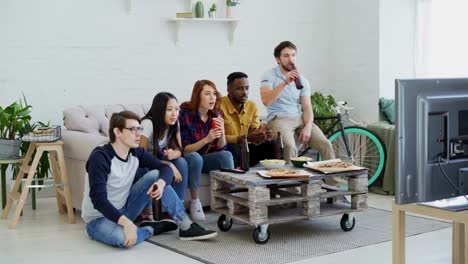 Gruppe-der-happy-Friends-Sportspiel-im-Fernsehen-zu-Hause-beobachten.-Sie-springen-und-schreien,-während-Sie-ihre-Lieblings-Team-gewinnen-Wettbewerb