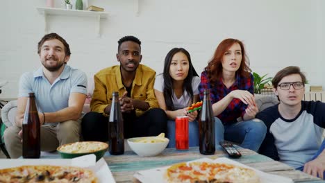 Multi-ethnische-Gruppe-von-Freunden-Sport-Fans-beobachten-Sport-im-Fernsehen-passen-zusammen-feiern-Ziel-der-Lieblingsmannschaft-während-Snacks-Essen-und-trinken-Bier-zu-Hause