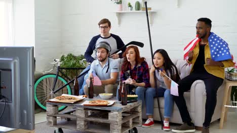 Multi-ethnic-group-of-friends-with-USA-national-flags-watching-sport-championship-on-TV-together-and-happy-about-winning-favourite-team-at-home