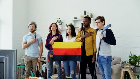 Multi-ethnischen-Gruppe-von-Freunden-hören-und-singen-der-deutschen-Nationalhymne-vor-gerade-Sport-Meisterschaft-im-Fernsehen-zusammen-zu-Hause