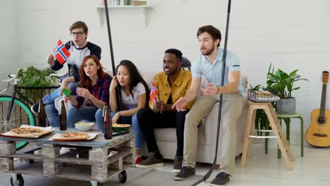 Grupo-de-jóvenes-amigos-de-deportes-aficionados-con-banderas-nacionales-noruegos-viendo-el-Campeonato-del-deporte-en-la-televisión-junto-y-feliz-por-ganar-el-equipo-favorito-en-casa