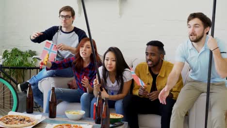 Diverse-group-of-friends-sport-fans-with-Norwegian-national-flags-watching-winter-sports-games-on-TV-together-cheering-up-favourite-team-at-home