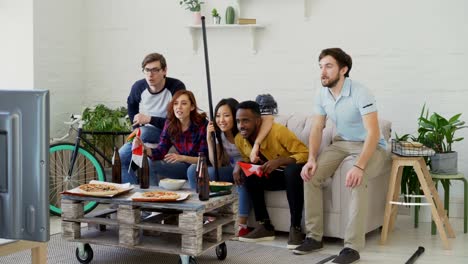 Multi-ethnische-Gruppe-von-Freunden-Sport-Fans-mit-Schweizer-Nationalflaggen-beobachten-Hockey-Meisterschaft-im-Fernsehen-zusammen-ihre-Lieblingsmannschaft-zu-Hause-Aufmunterung