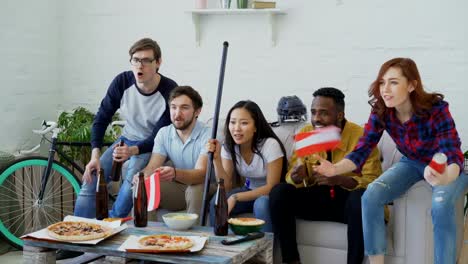 Multi-ethnic-group-of-friends-sports-fans-with-Austrian-national-flags-watching-hockey-championship-on-TV-together-cheering-up-their-favourite-team-at-home