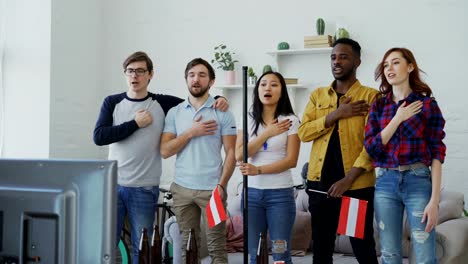 Multi-ethnischen-Gruppe-von-Freunden-hören-und-singen-österreichische-Nationalhymne-vor-gerade-Sport-Meisterschaft-im-Fernsehen-zusammen-zu-Hause