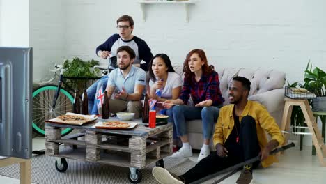 Multi-étnico-grupo-de-amigos-fans-de-los-deportes-con-banderas-nacionales-británicas-viendo-el-Campeonato-de-hockey-en-la-televisión-animando-a-su-equipo-favorito-en-casa